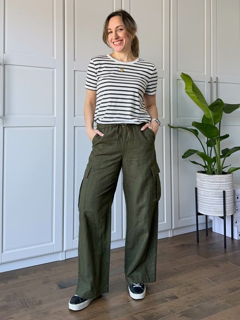 Woman posing wearing a black/white striped t-shirt, wide leg olive green linen pants and black sneakers.