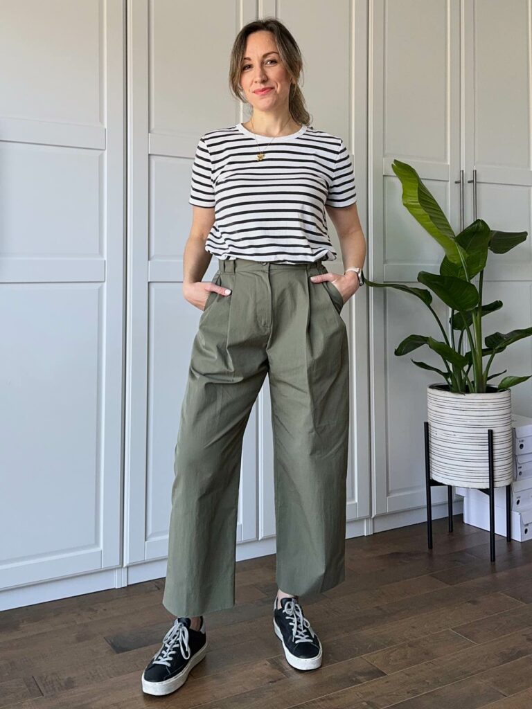 Woman posing wearing a black/white striped t-shirt, barrel shaped olive green pants and black sneakers.