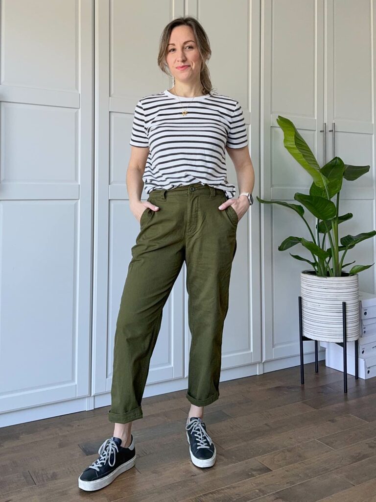 Woman posing wearing a black/white striped t-shirt, olive green pants and black sneakers.