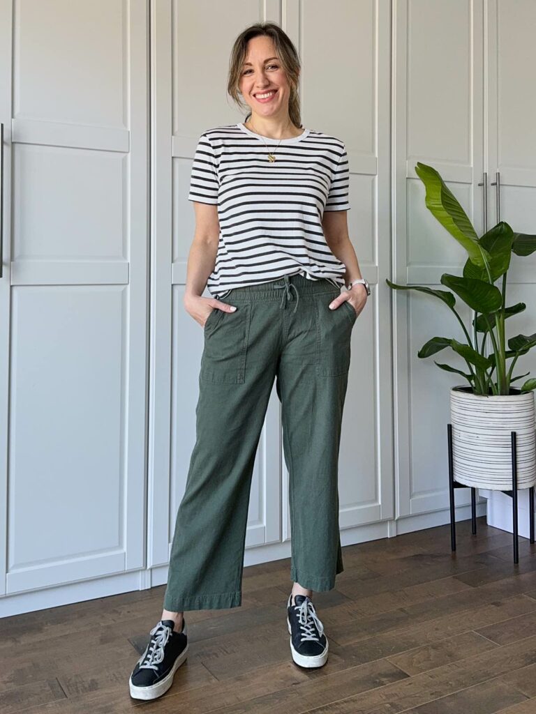 Woman posing wearing a black/white striped t-shirt, cropped linen olive green pants and black sneakers.