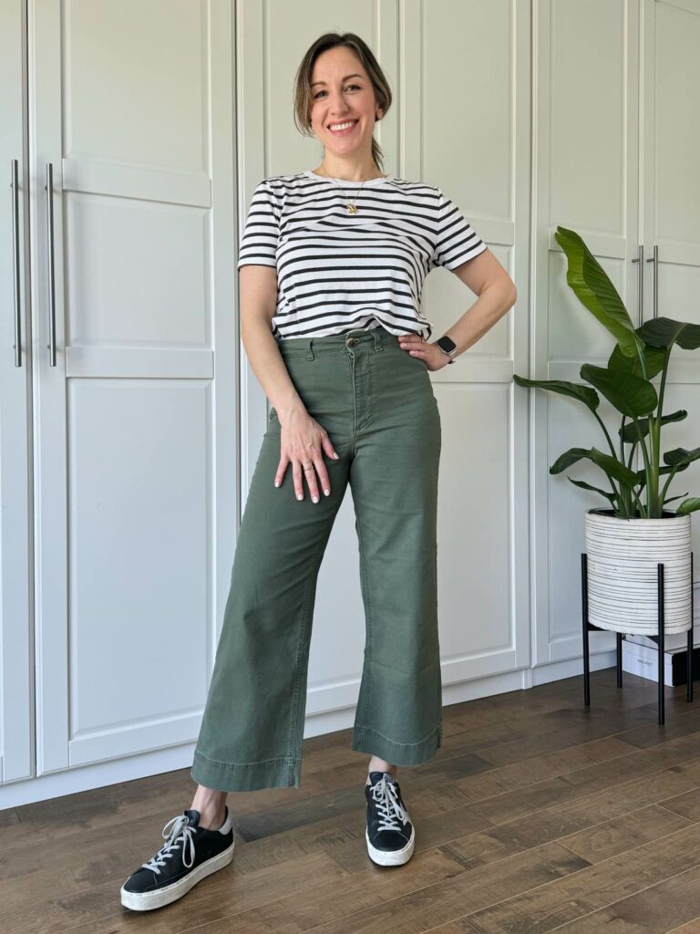 Woman posing wearing a black/white striped t-shirt, cropped wide leg olive green pants and black sneakers.