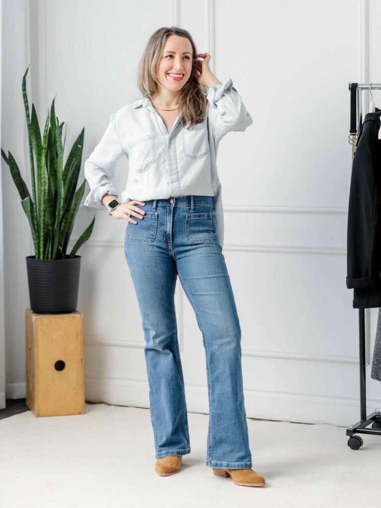 Woman posing in front of a white closet wearing a light denim shirt styled with darker jeans.