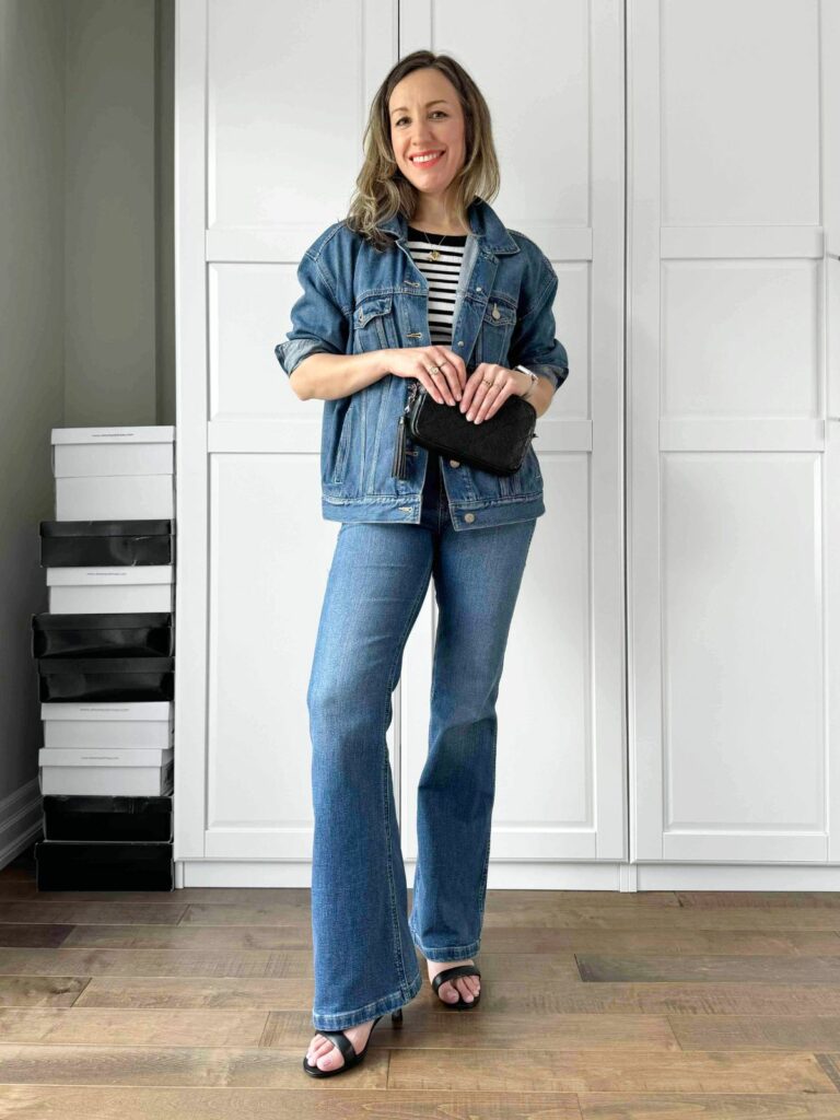 Woman posing in front of a white closet wearing a denim jacket over the striped top styled with jeans.