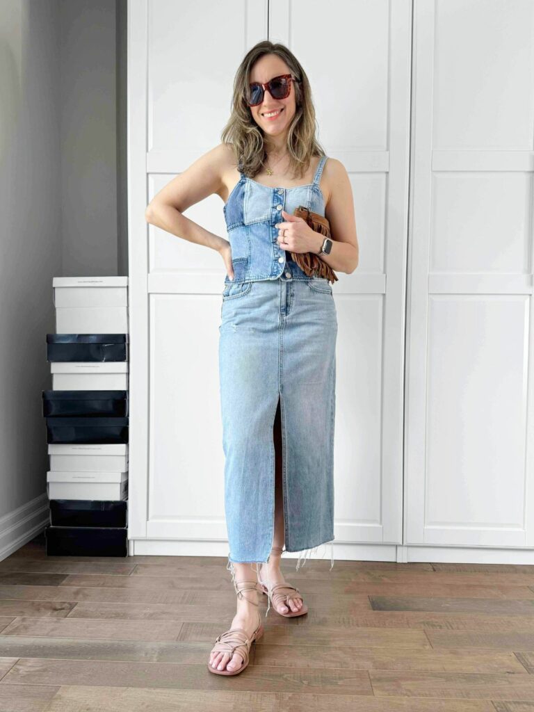 Woman posing in front of a white closet wearing a patchwork denim corset top styled with midi denim skirt.