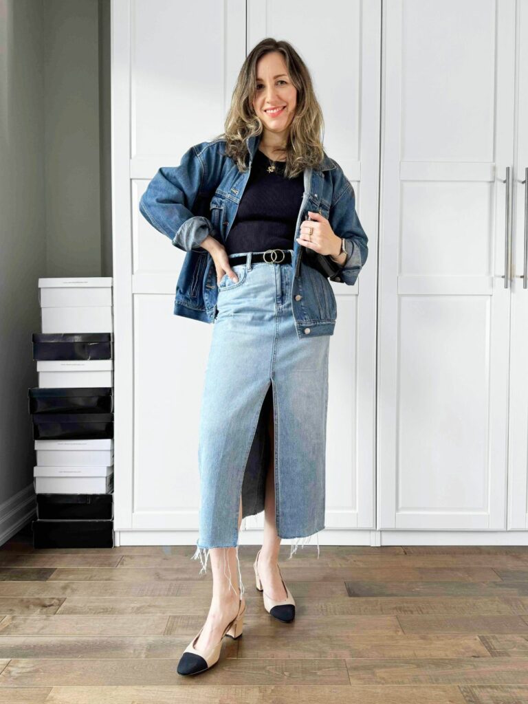 Woman posing in front of a white closet wearing a denim jacket over the black top styled with midi denim skirt.