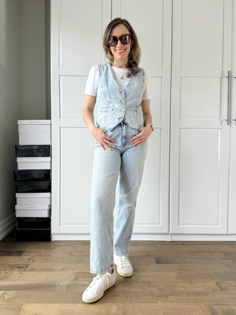 Woman posing in front of a white closet wearing a light denim vest styled with light jeans and white T-shirt.