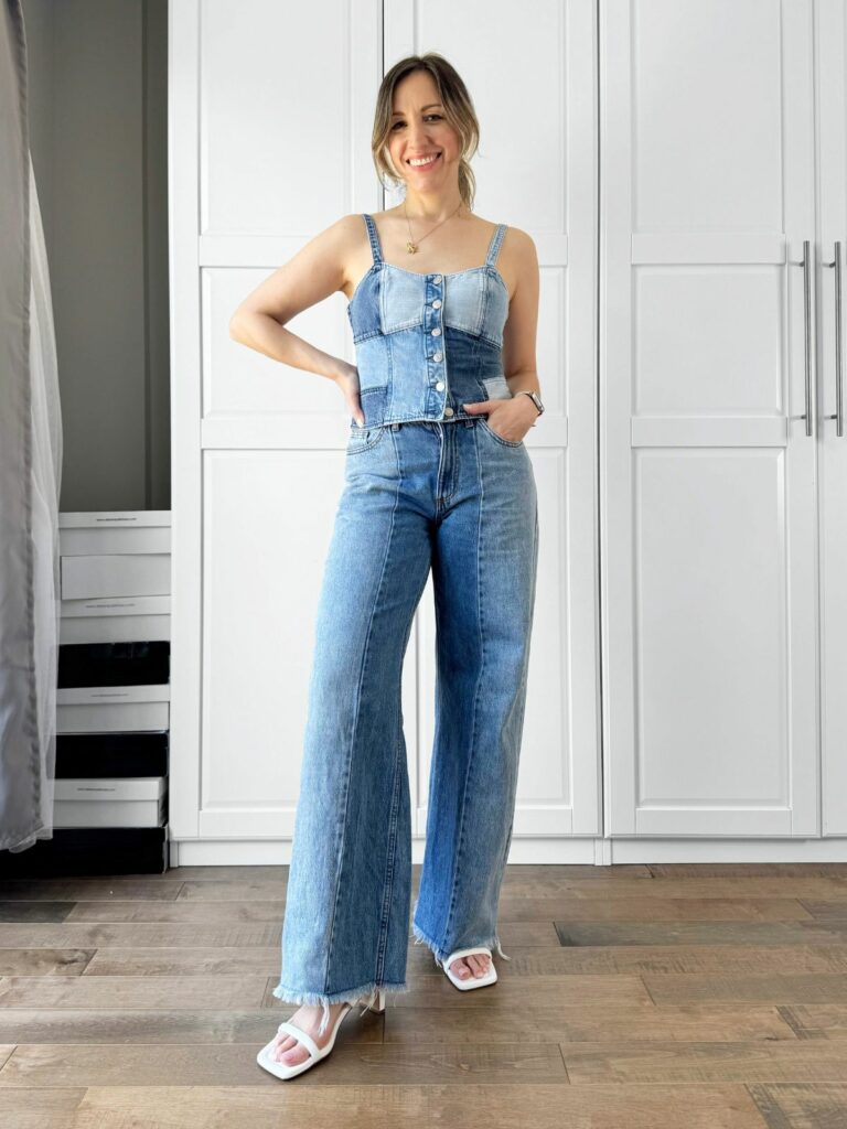 Woman posing in front of a white closet wearing a patchwork denim corset top styled with two-tone wide leg jeans.