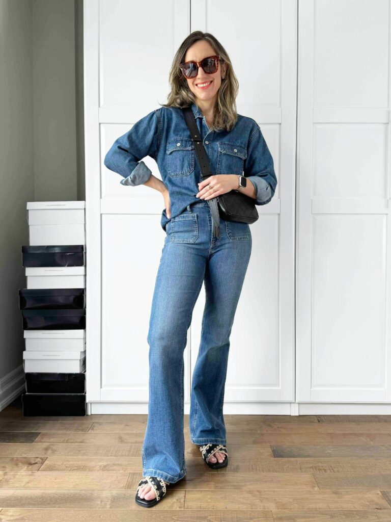 Woman posing in front of a white closet wearing a dark denim shirt styled with jeans.