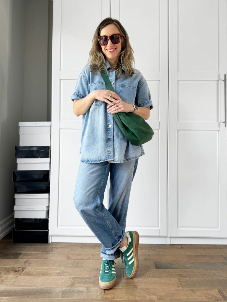 Woman posing in front of a white closet wearing a denim shirt styled with cuffed jeans.