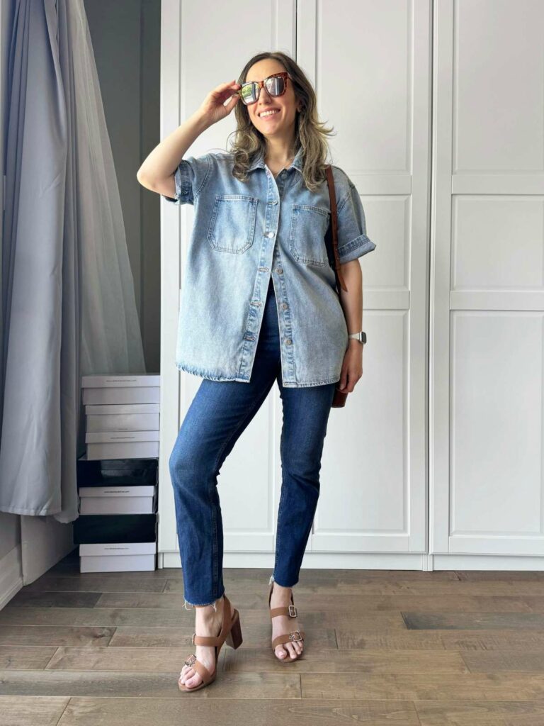 Woman posing in front of a white closet wearing a light denim shirt with dark denim skinny jeans with brown accessories.