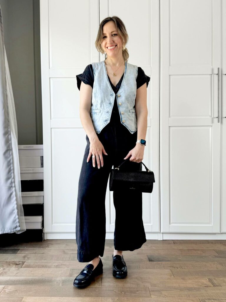 Woman posing in front of a white closet wearing a light denim vest styled with black tee and black pants.