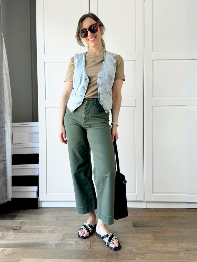 Woman posing in front of a white closet wearing a light denim vest styled with beige tee and dark green pants.