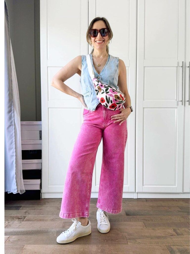 Woman posing in front of a white closet wearing a light denim vest styled with pink jeans.