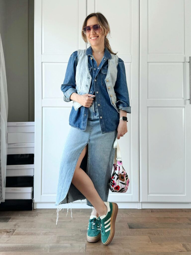 Woman posing in front of a white closet wearing a light denim vest styled with denim shirt and midi denim skirt.