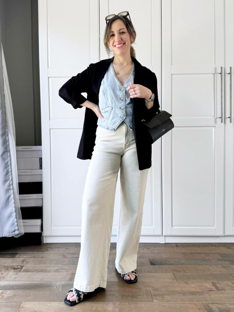 Woman posing in front of a white closet wearing a light denim vest styled with black blazer and light beige pants.