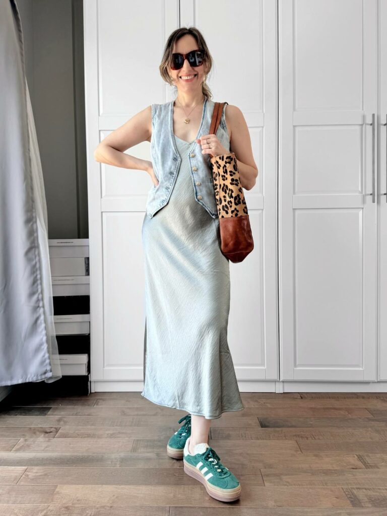 Woman posing in front of a white closet wearing a light denim vest styled with midi light grey dress.