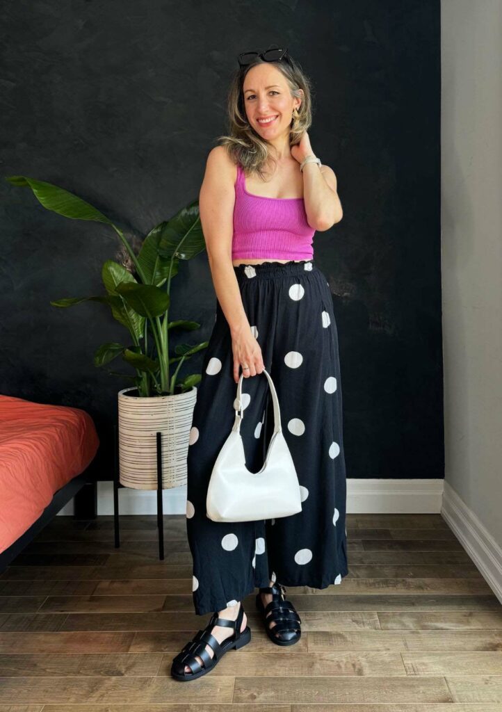 Woman posing wearing a pink crop top with black wide leg pants featuring large white polka dots.