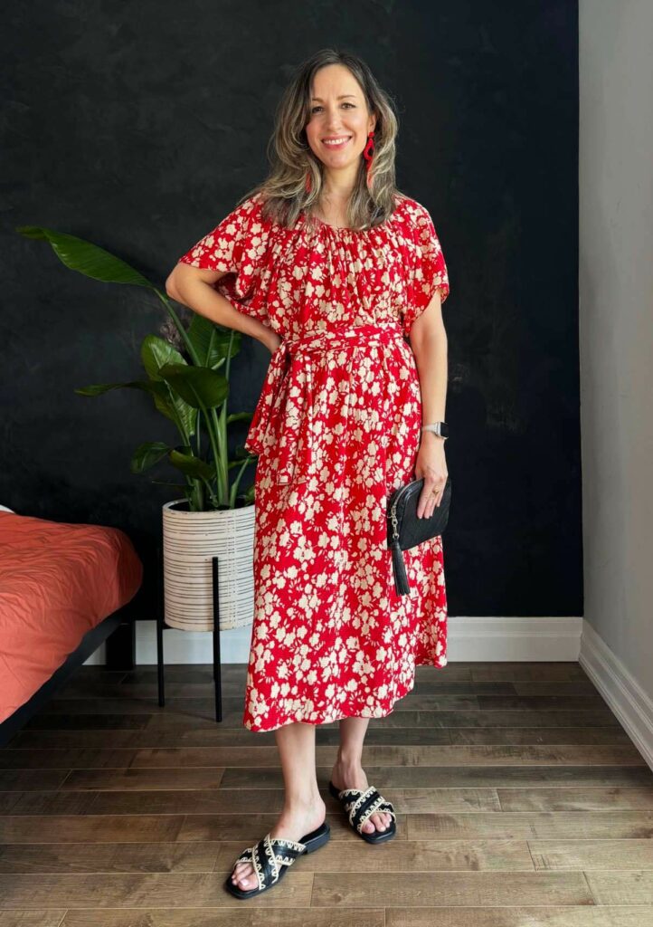 Woman posing wearing a red silk dress with white floral pattern.