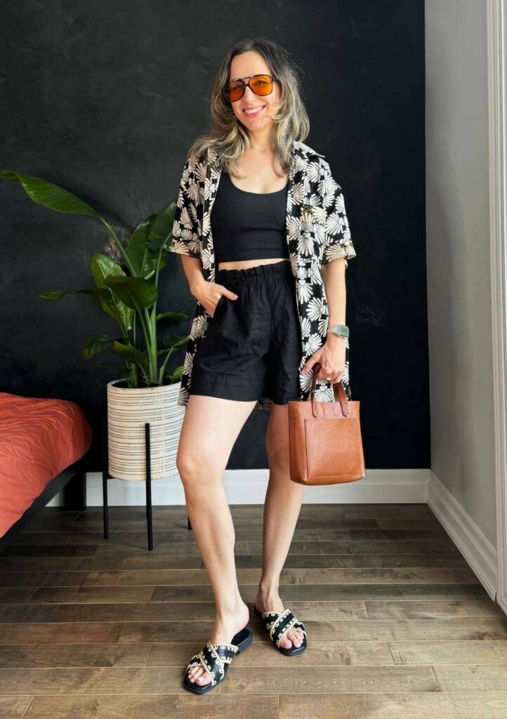 Woman posing wearing a black crop top with black linen shorts and loose shirt with floral print in black and white.