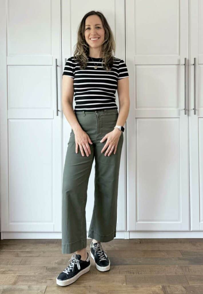 Woman posing wearing olive green pants with black and white stripes top.