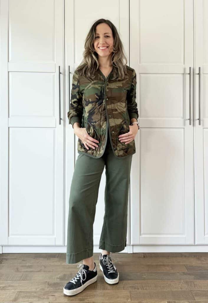 Woman posing wearing olive green pants with camouflage print jacket.