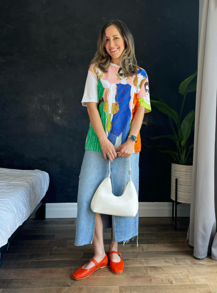 Woman posing wearing a graphic t-shirt outfit with a denim skirt.