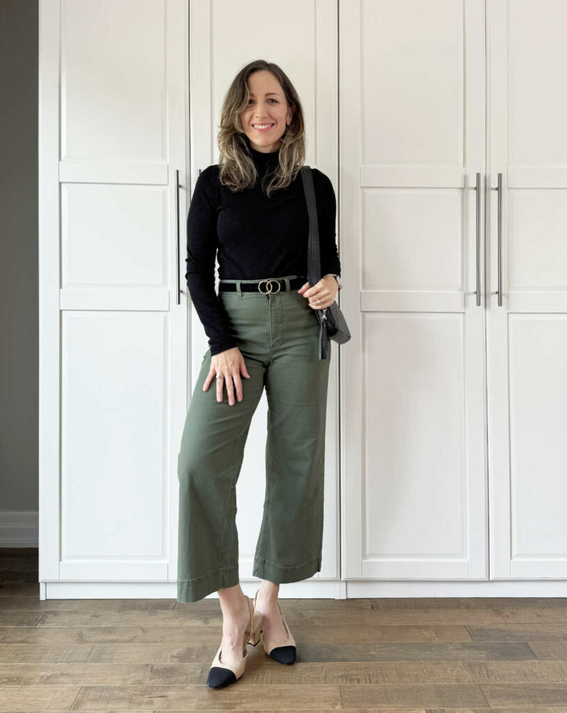 Woman posing wearing business casual outfit consisting of olive green pants for fall with a black turtleneck & slingback pumps.