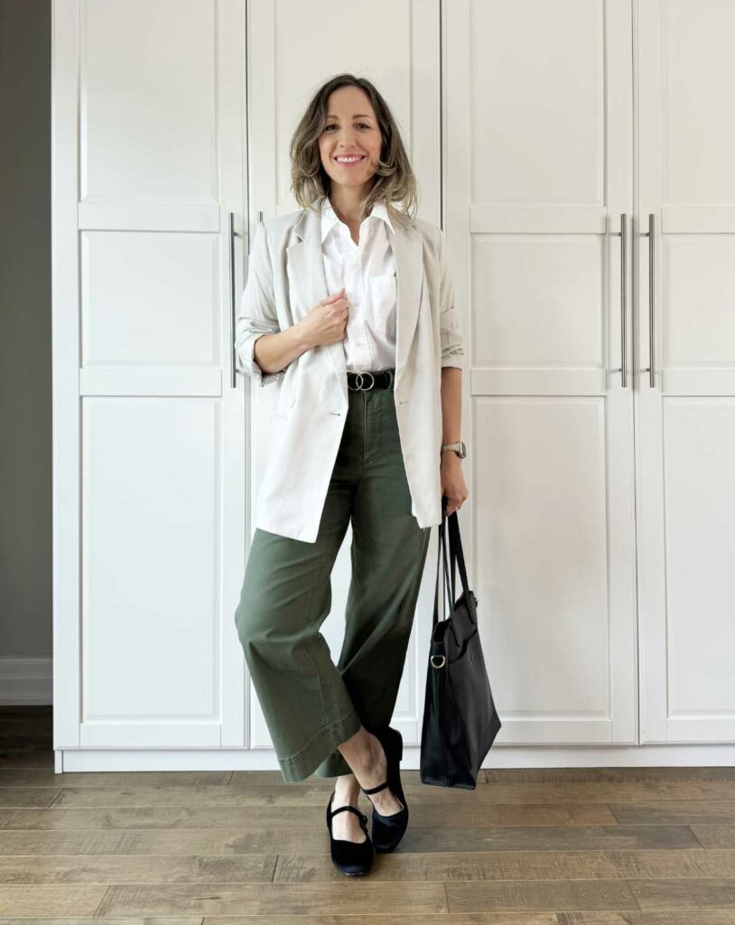 Woman posing wearing business casual outfit consisting of olive green pants for fall with a blazer, white shirt + flats.