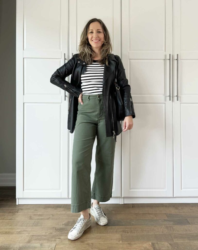 Woman posing wearing olive green pants for fall with striped tee and leather jacket.