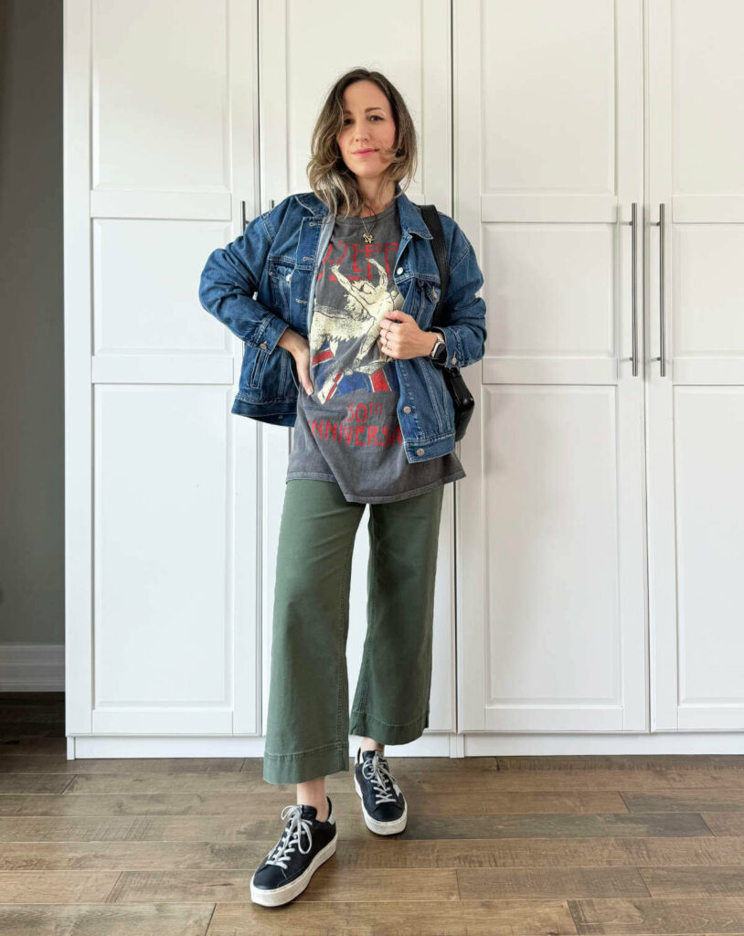 Woman posing wearing olive green pants for fall with denim jacket, graphic tee + sneakers.