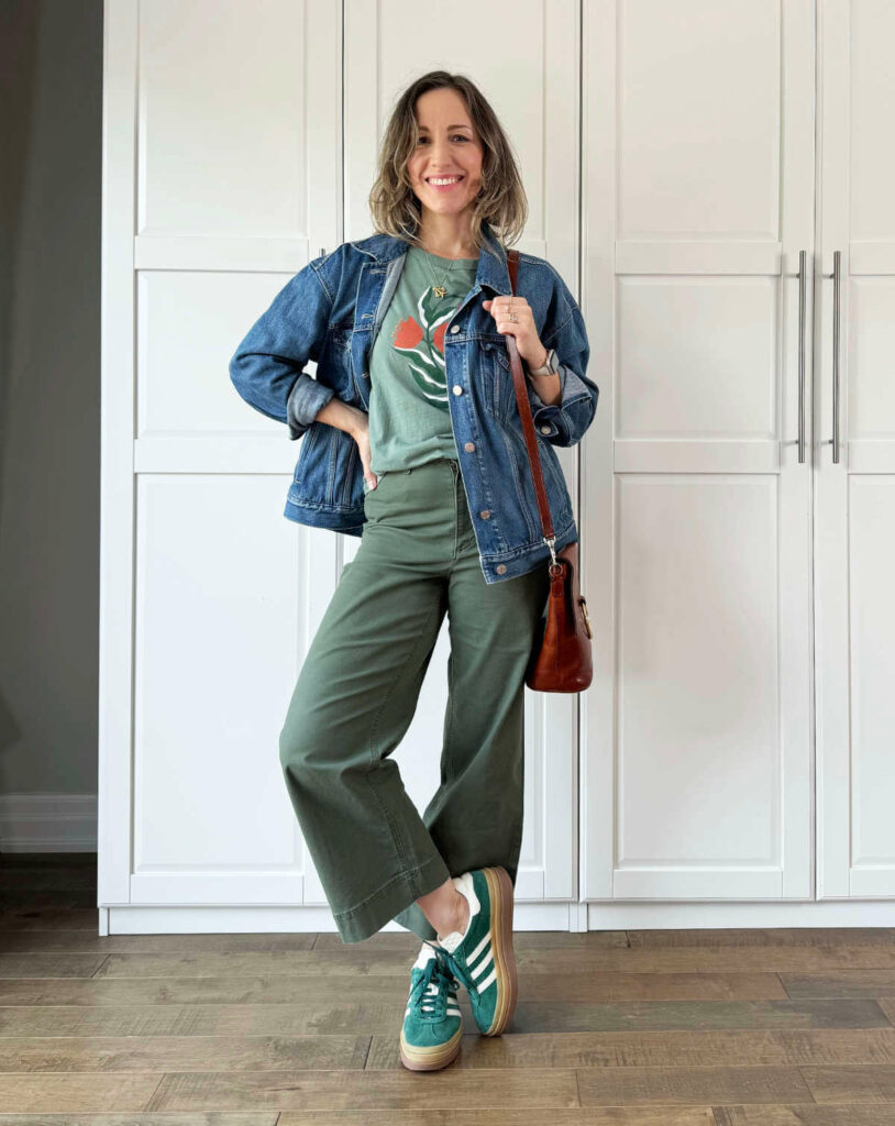 Woman posing wearing olive green pants for fall with denim jacket, graphic tee + sneakers.