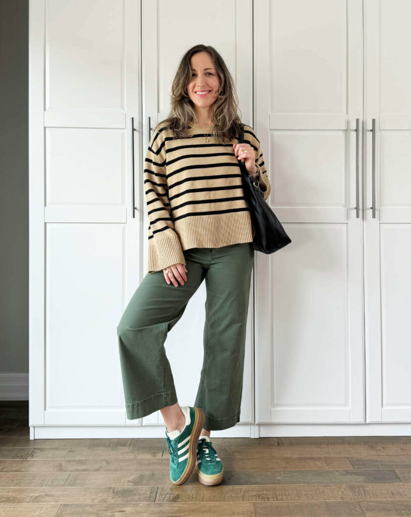 Woman posing wearing olive green pants for fall with a tan striped crew neck sweater + green sneakers.